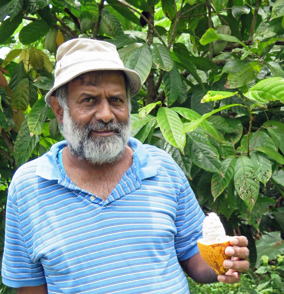 Naresh (Bobby) Shankaran is  holding a cocoa pod in his left hand. 